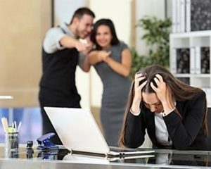 Una donna al computer con le mani tra i capelli e alle spalle due colleghi che si divertono 