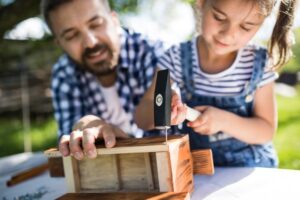 Un papà passa del tempo in giardino con la sua bambina costruendo con legno martello e chiodi